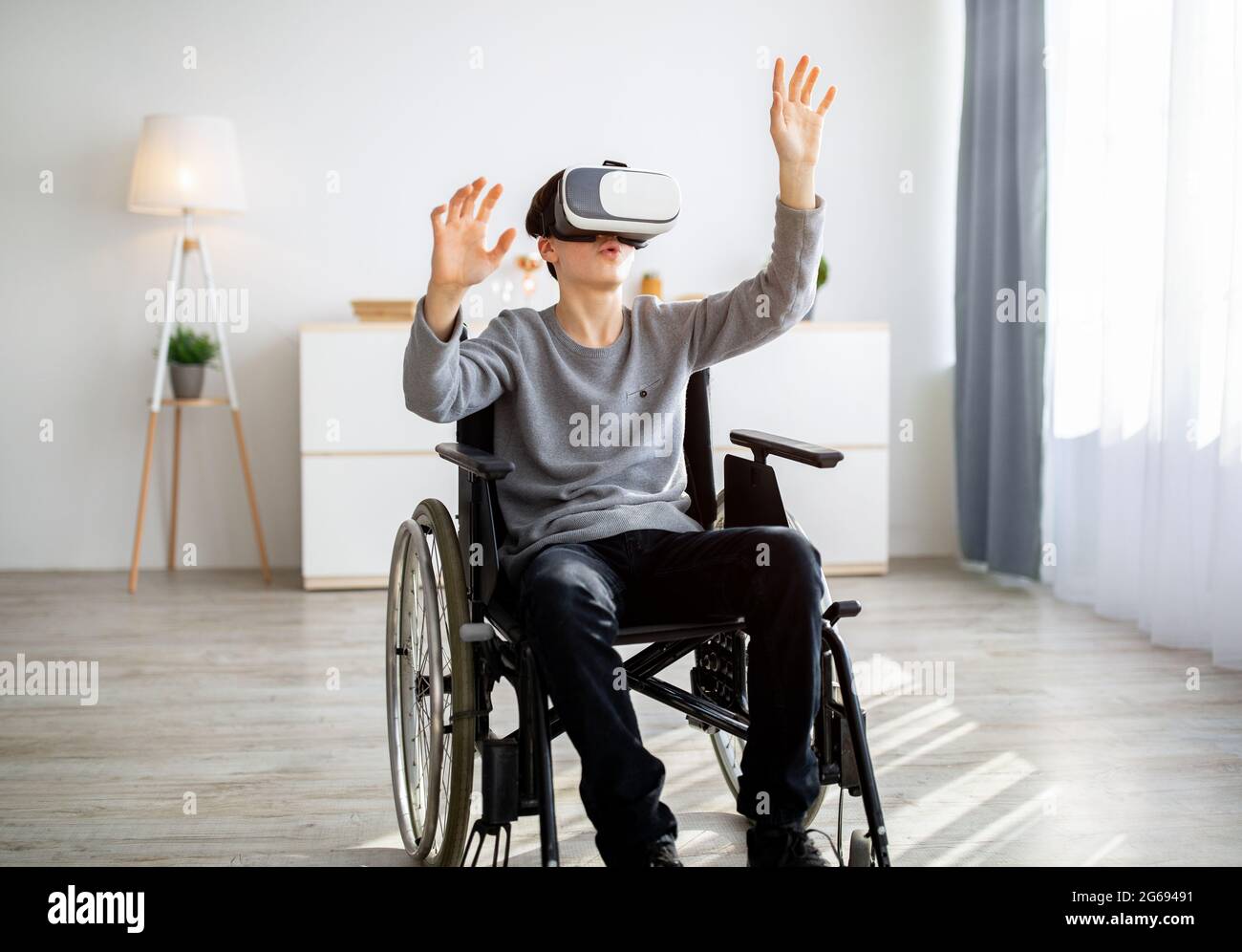 Handicapped teenager in wheelchair wearing VR headset, exploring augmented reality at home Stock