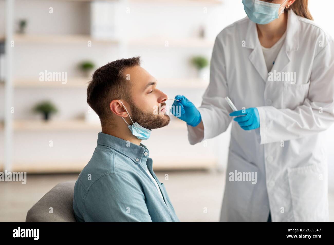 Covid diagnostic procedure. Doctor making nasal PCR test for young Caucasian man, using sterile swab stick at home Stock Photo