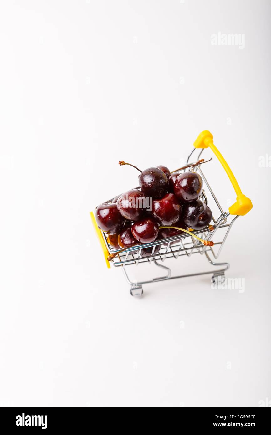 Cherry in a miniature (small) grocery cart for a supermarket. Toy cart with berries on a white background. Close-up, Copy space for text, top view. Stock Photo