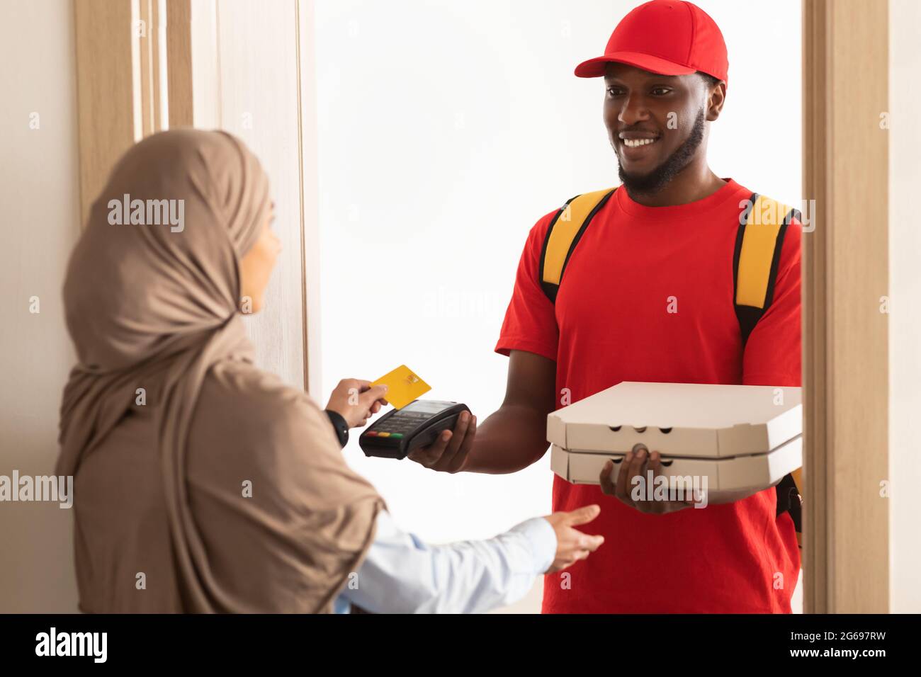 Smiling deliveryman holding POS machine, woman paying with card Stock Photo