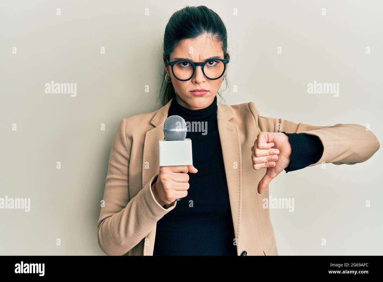 Young hispanic woman holding reporter microphone with angry face ...