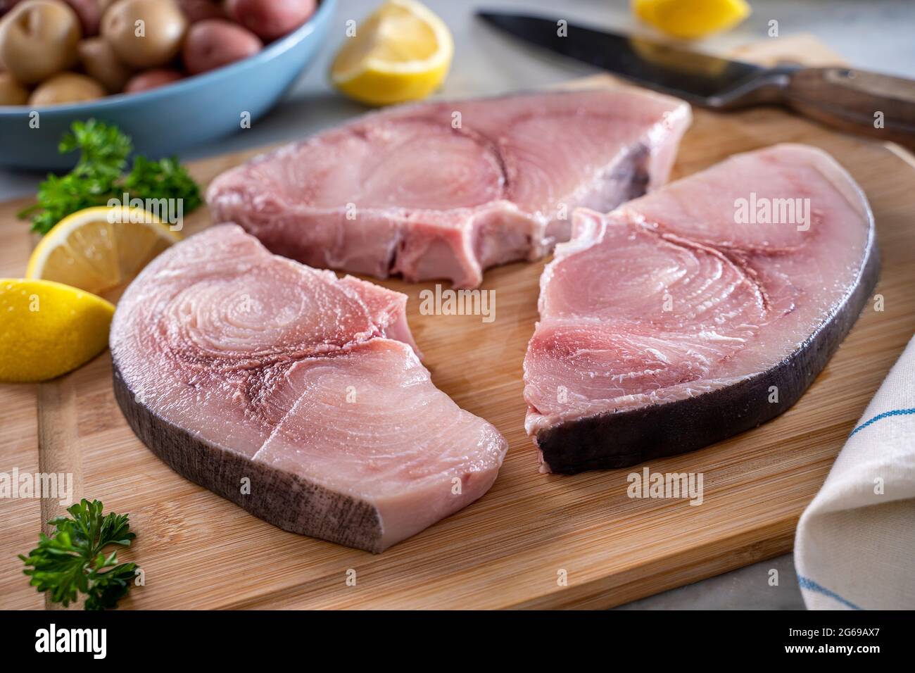 Fresh raw swordfish steaks being prepared on a bamboo cutting board. Stock Photo