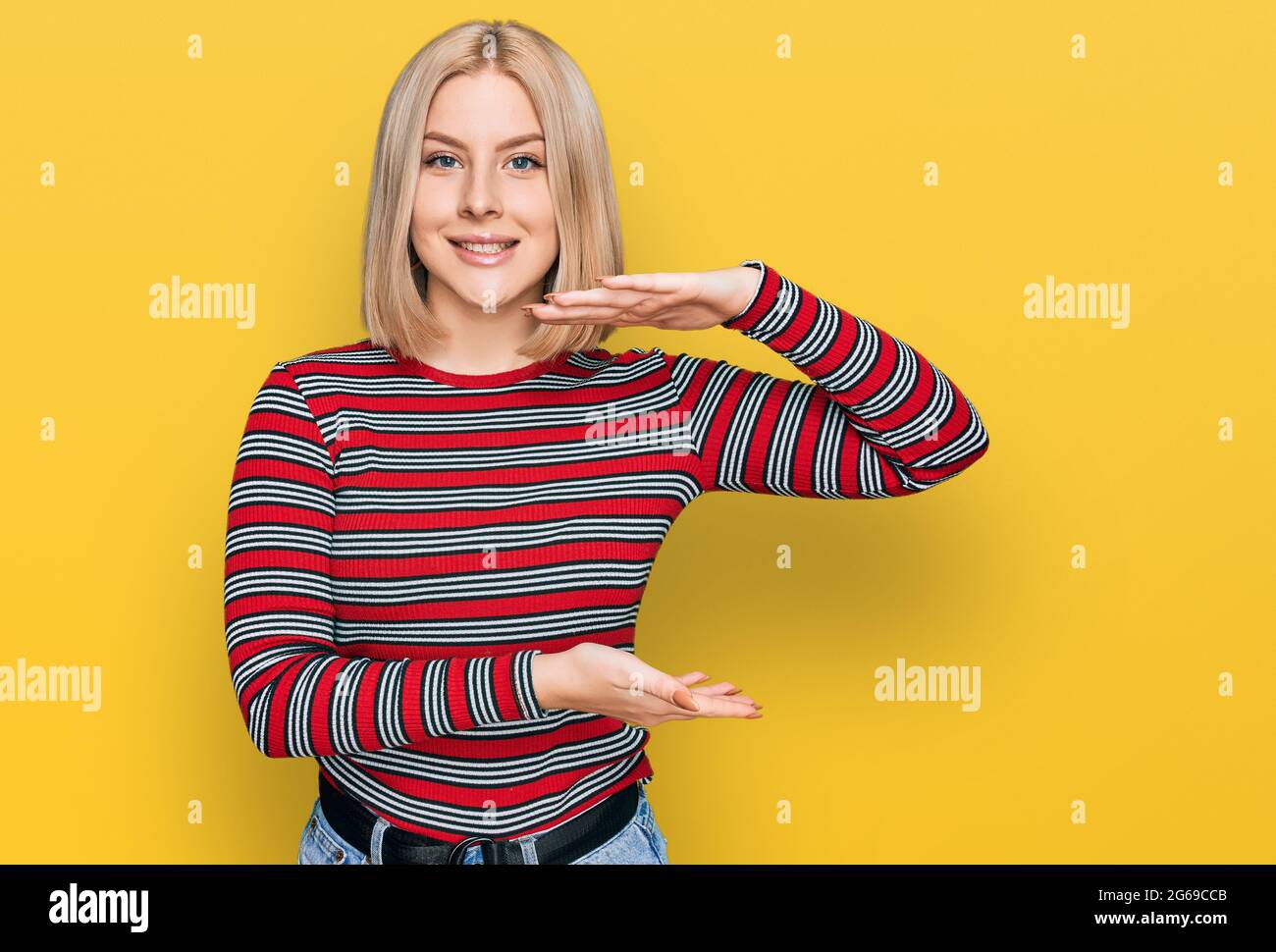 Young blonde woman wearing casual clothes gesturing with hands showing big and large size sign, measure symbol. smiling looking at the camera. measuri Stock Photo