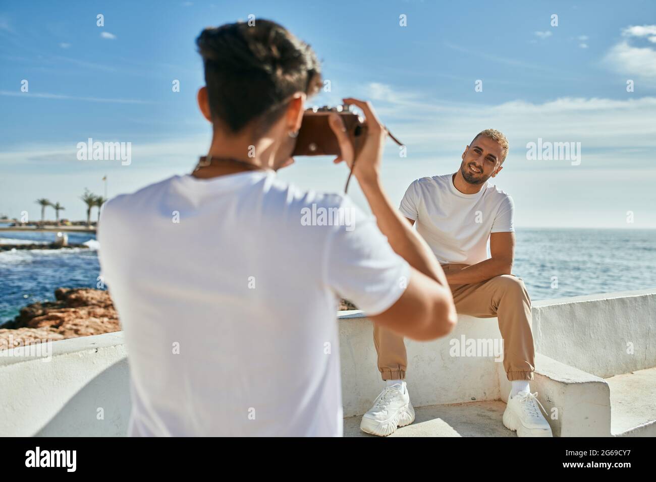 Man taking photos of his boyfriend in front of the sea. Stock Photo