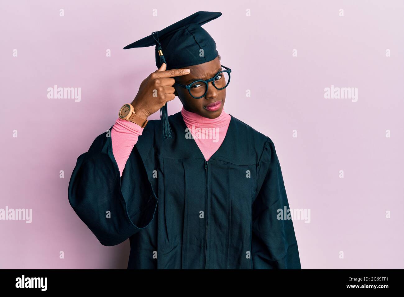 Young african american girl wearing graduation cap and ceremony robe pointing unhappy to pimple on forehead, ugly infection of blackhead. acne and ski Stock Photo