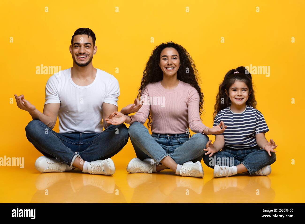 Cheerful Middle-Eastern Parents And Daughter Sitting In Lotus Position On Yellow Background Stock Photo