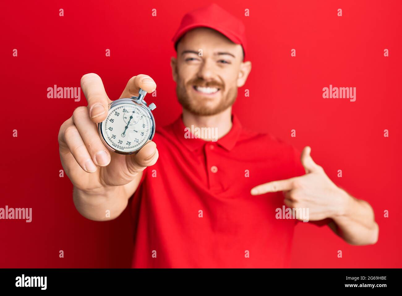 Young redhead man wearing delivery uniform and countdown clock pointing ...