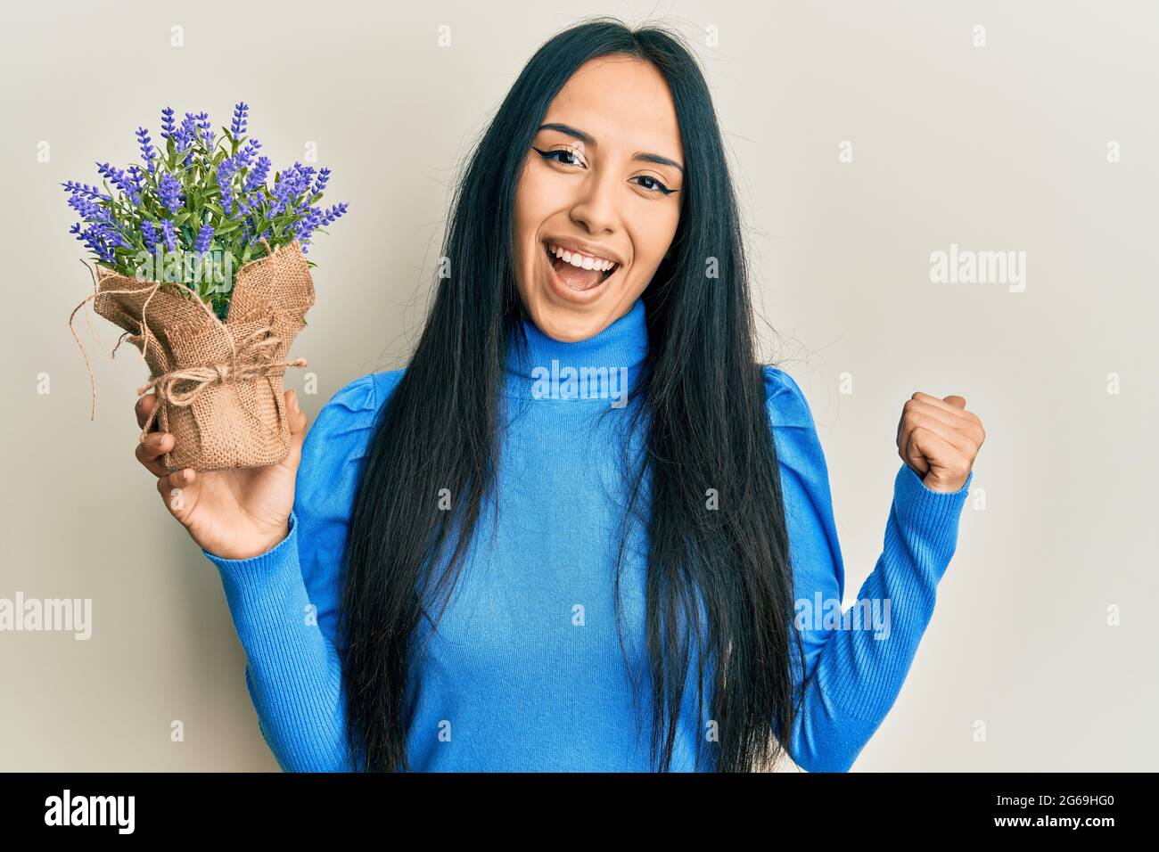 Young hispanic girl holding lavender plant pointing thumb up to the ...
