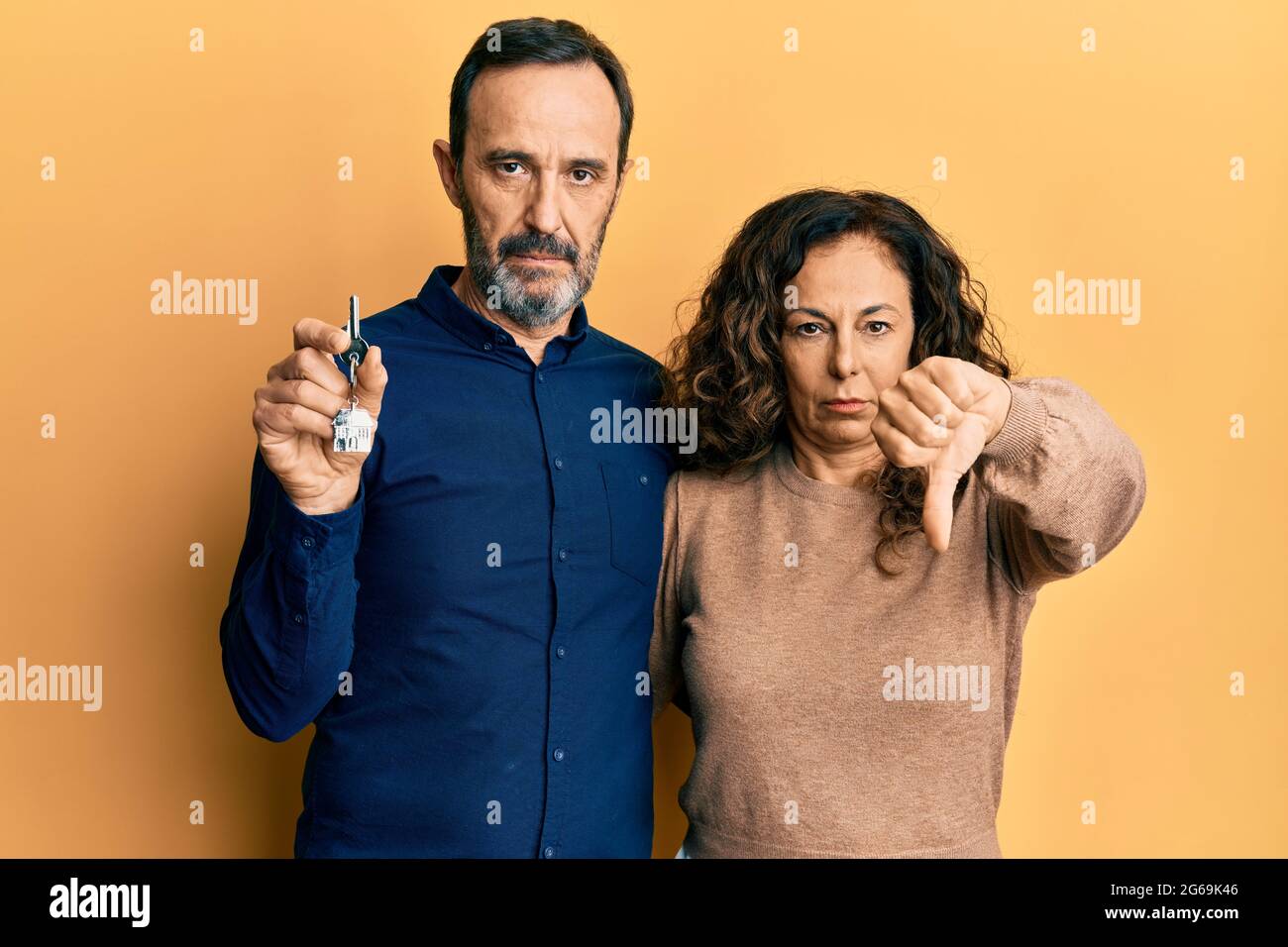 Middle age hispanic couple holding keys of new home with angry face ...
