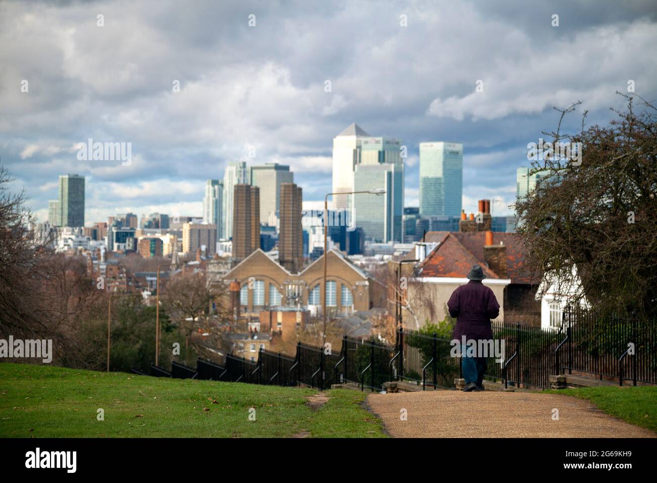 Man walking across Greenwich park with view of Canary Wharf and Greenwich power station on the background - London. Stock Photo