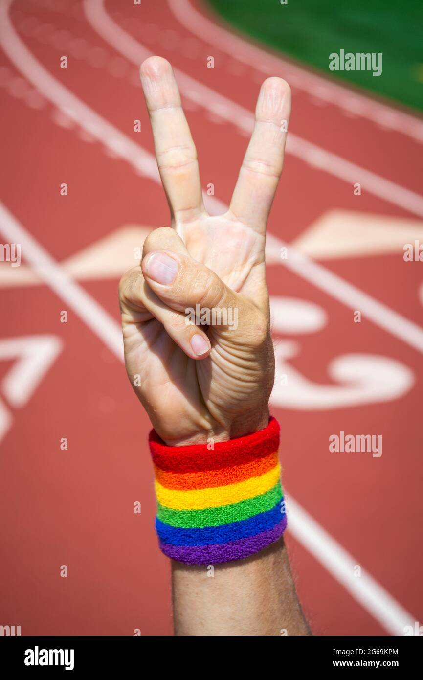 Athlete with gay pride rainbow wrist sweatband making a v-sign for victory with hand at a running track Stock Photo