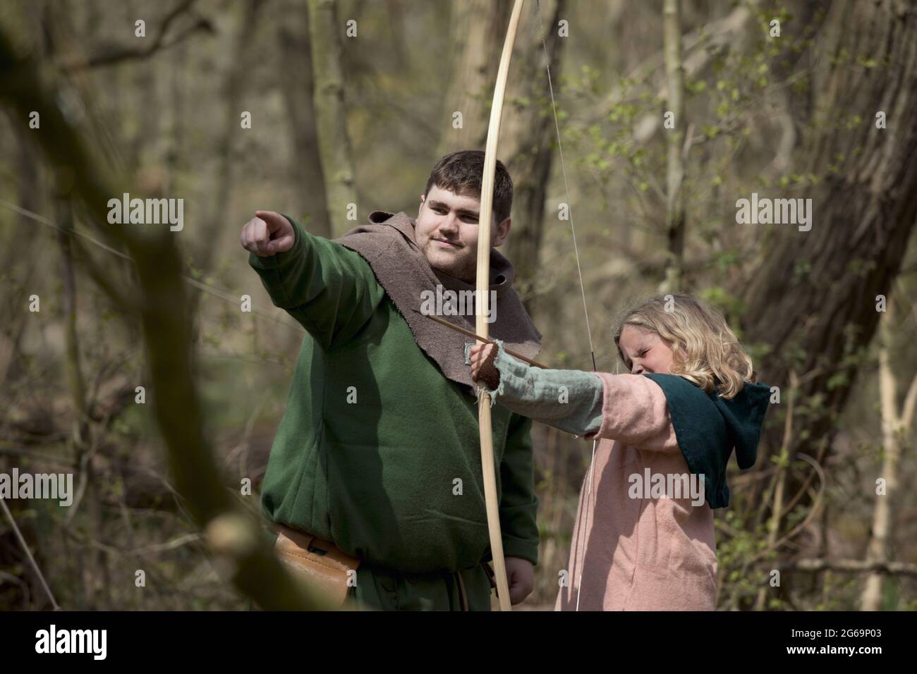 Interpretation of young girl being taught how to shoot a long bow in early medieval Britain. Stock Photo