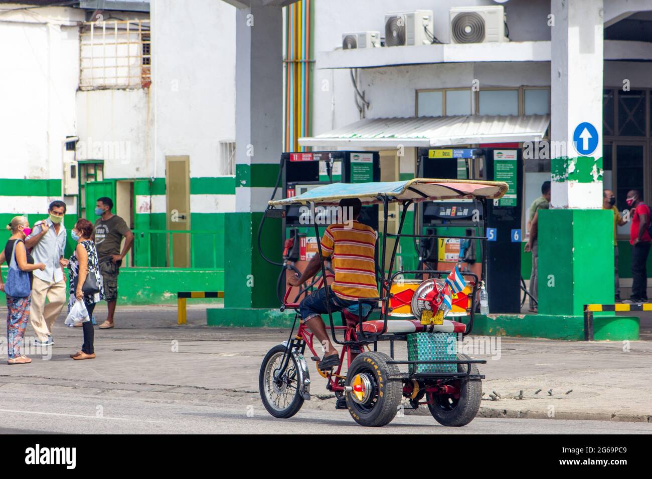 A pedicab or bici-taxi driving on a Santiago de Cuba city street. People with protective face masks are seen in the scene. Stock Photo
