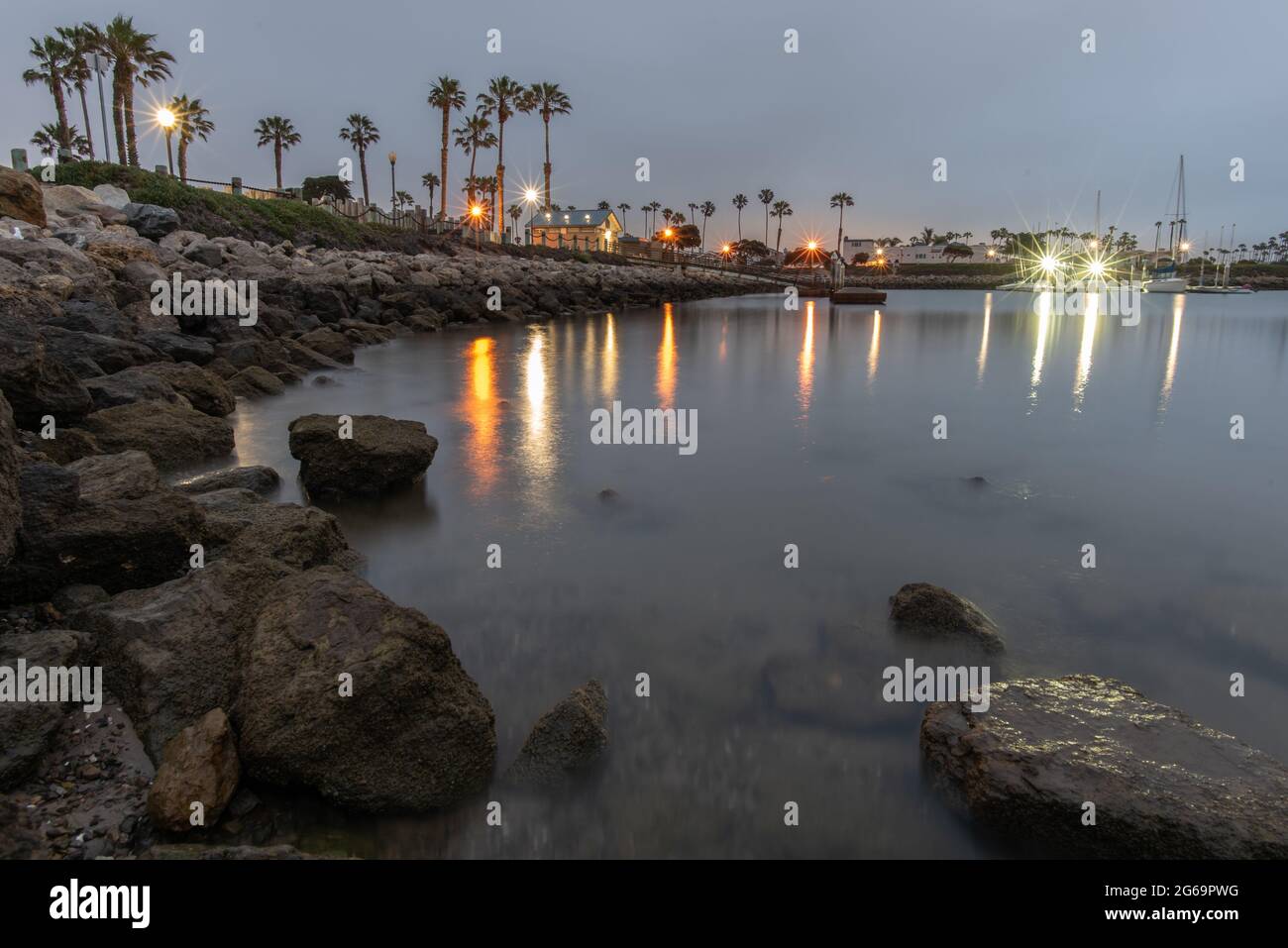 Smooth surface on the ocean cove water with the reflection of lights and rocks in the morning. Stock Photo