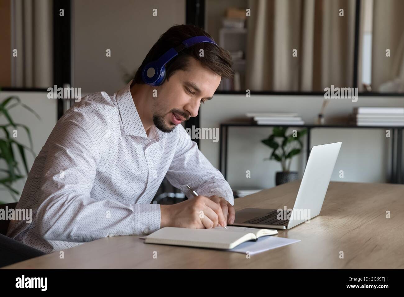 Employee in headphones taking notes, watching webinar in office Stock Photo