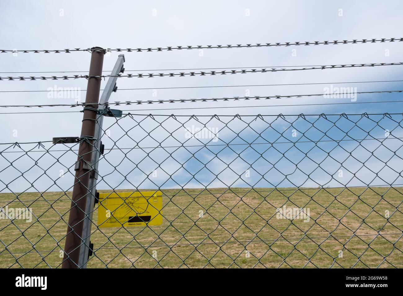 Barbed wire fence with dangerous electrical voltage power line on the border Stock Photo