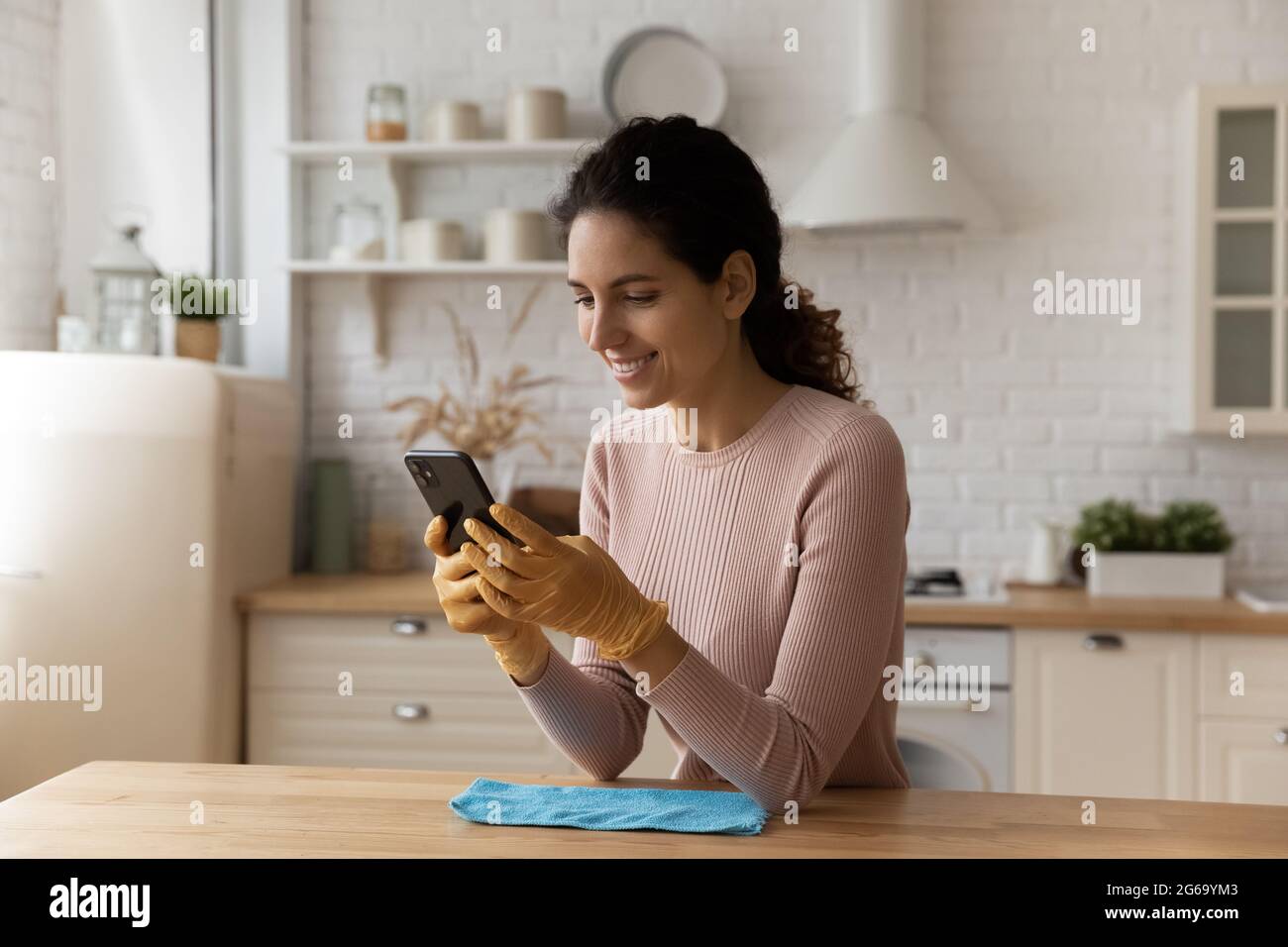 Distracted from cleaning young woman sending message on smartphone. Stock Photo