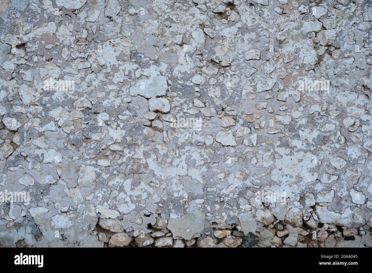 Old traditional limewashed stone wall with peeling plaster, white rustic background or texture Stock Photo