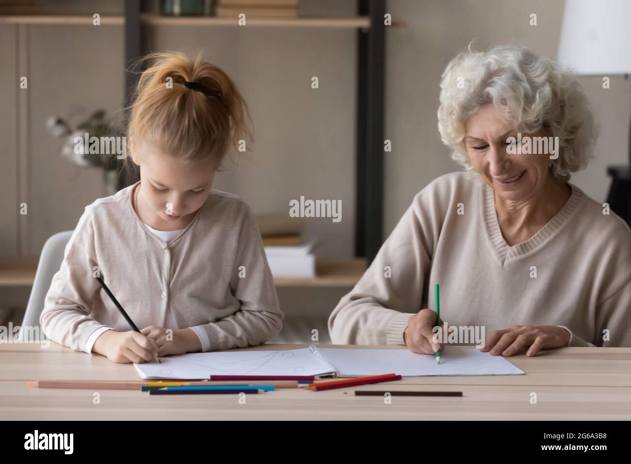 Caring senior grandmother assist preteen grandchild to paint coloring book Stock Photo