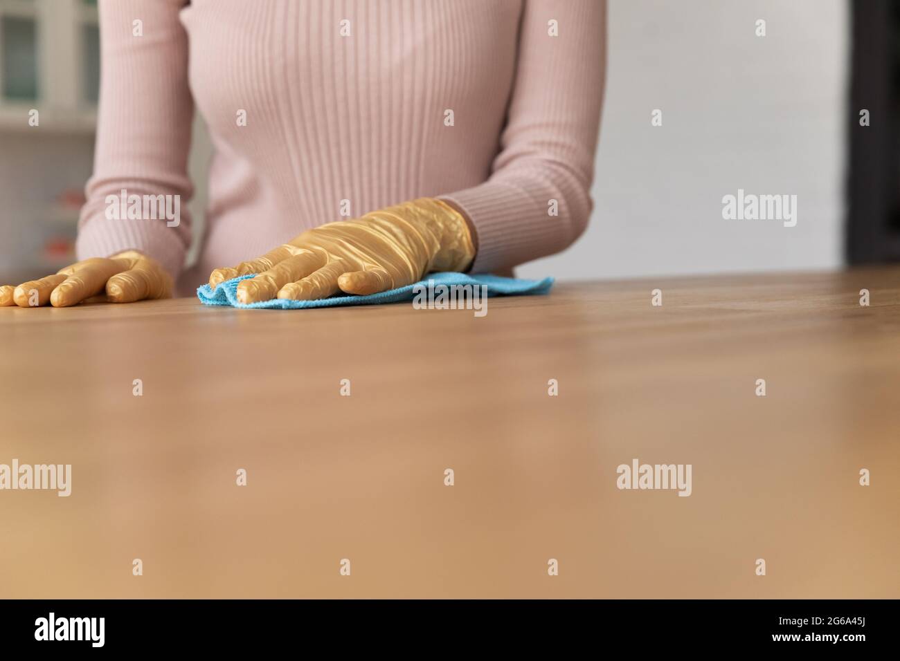 Close up young woman cleaning wooden table in gloves. Stock Photo