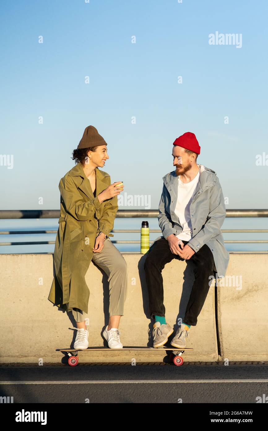 Young couple of hipster skateboarders relax after skateboarding training sitting on concrete bridge Stock Photo