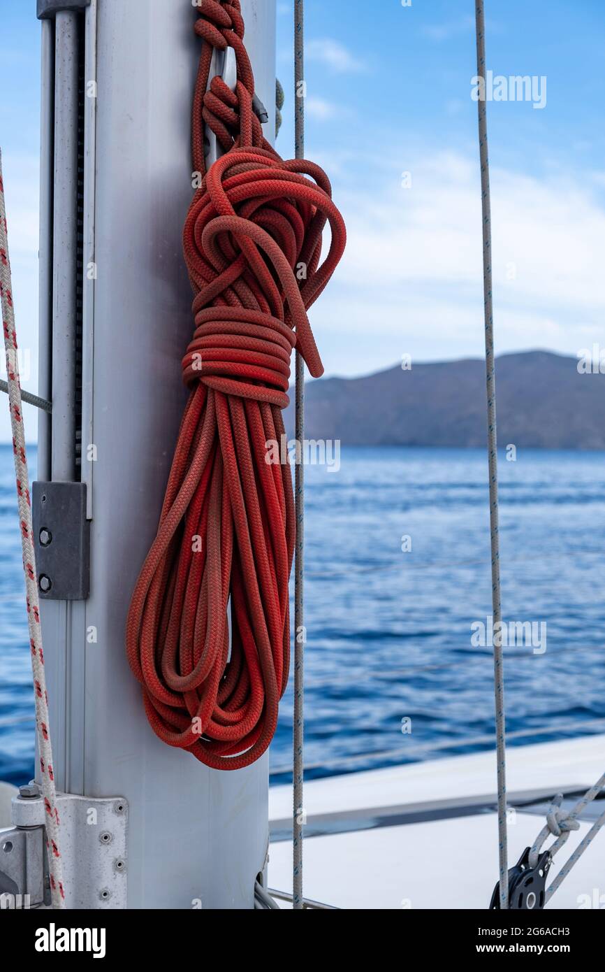 Mooring ropes on the sailing boat, blur seascape background. Red color yachting rope on the ship mast. Closeup view, vertical. Sailboat cruise in Aege Stock Photo