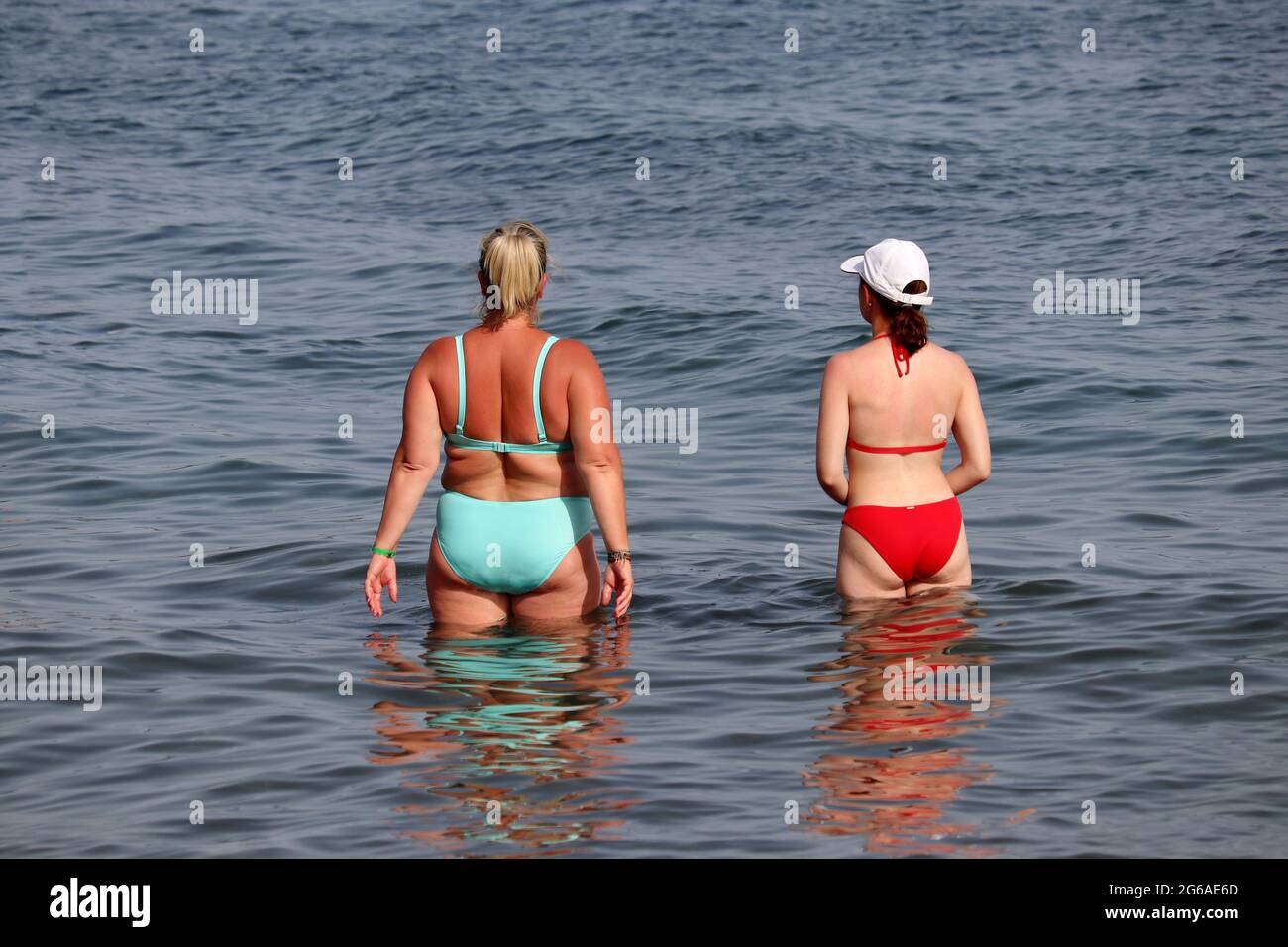 Fat and slim girls in bikini going to swim in sea water, rear view. Two girlfriends on a summer beach, overweight and dieting concept Stock Photo