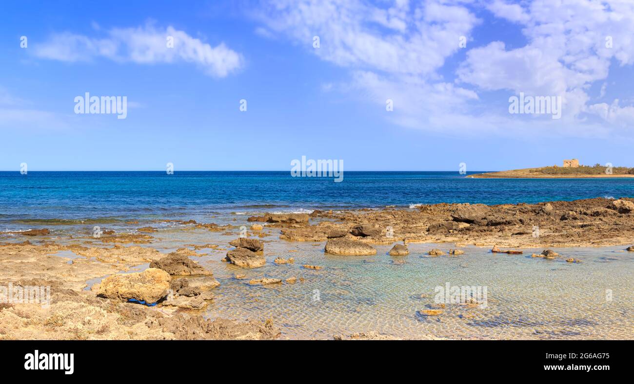Apulia seascape: rocky beach in Torre Guaceto Nature reserve, Italy. In the background sandy beach width dune and watchtower. Stock Photo