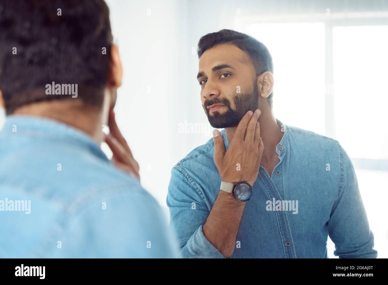 Curious thoughtful indian man touching beard on face looking at mirror  Stock Photo - Alamy