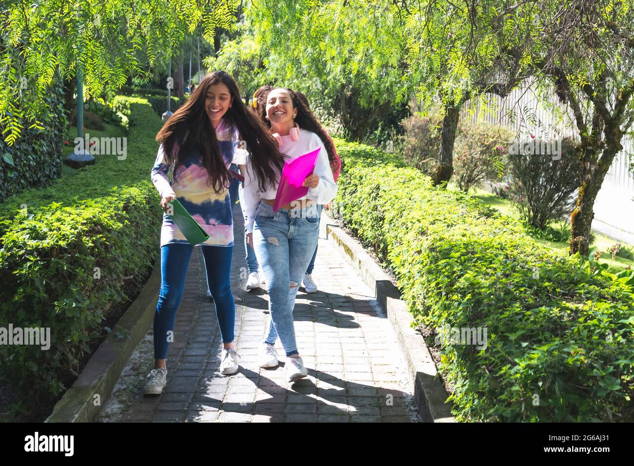 Two Latina friends go cheerfully on their way to high school on a sunny morning. Education concept Stock Photo