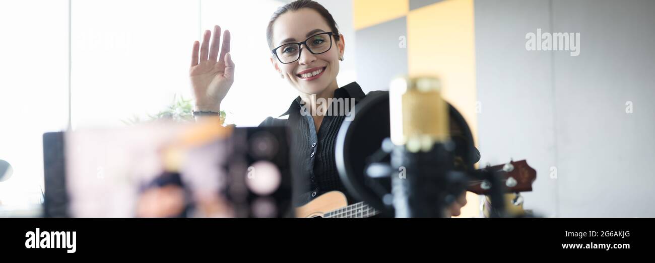 Woman in wheelchair holding ukulele and waving hand to camera Stock Photo