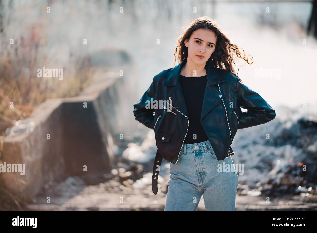Outdoor portrait of a beautiful teen brunette girl in the black leather jacket with smoke in the background Stock Photo