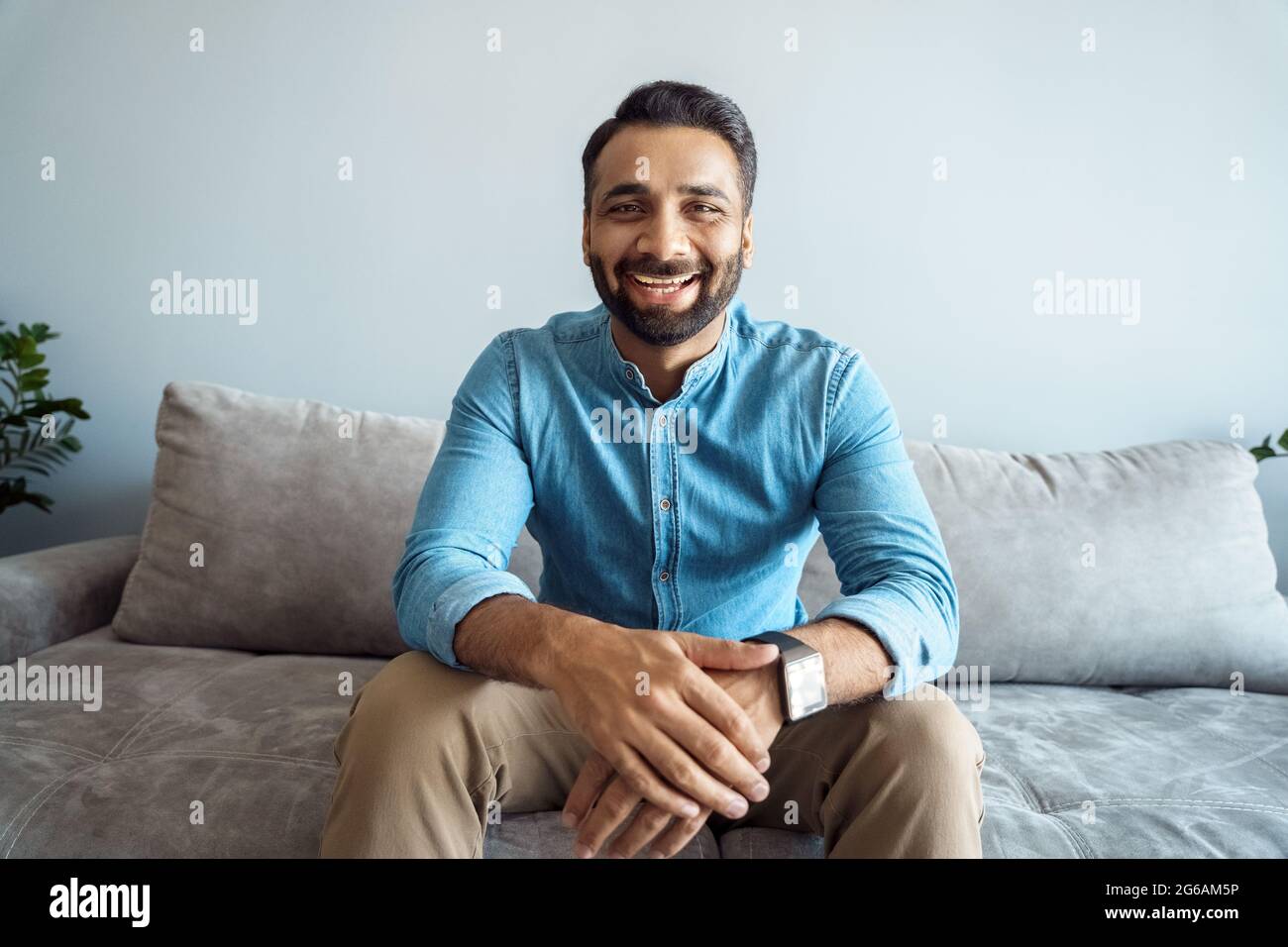 Portrait of indian man toothy smiling to camera sitting on sofa webcam view Stock Photo