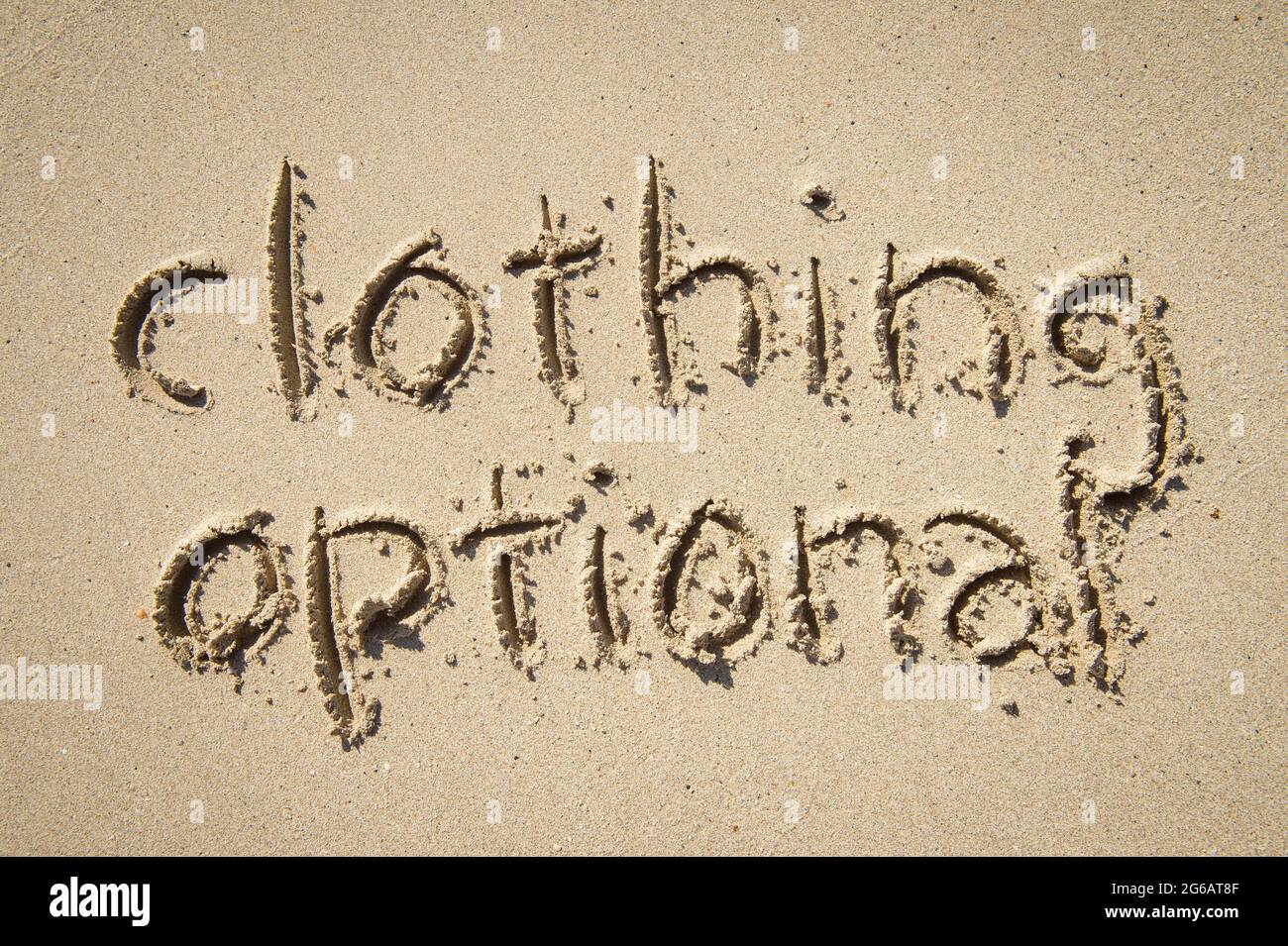 Clothing optional nudist message handwritten in simple text on smooth sand beach Stock Photo
