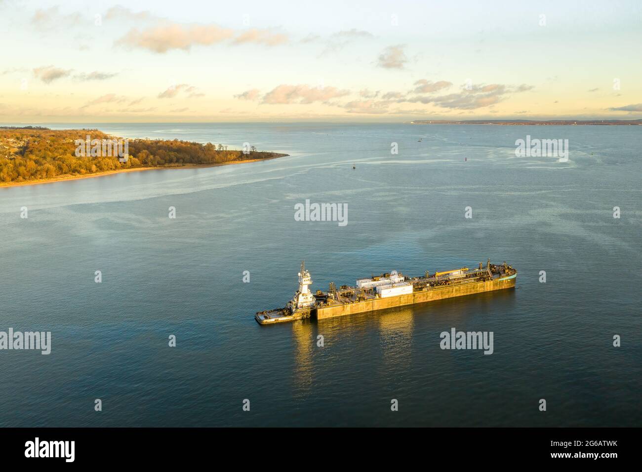 Aerial of large barge in water at sunset with a pink sky and a piece of land in view. Stock Photo