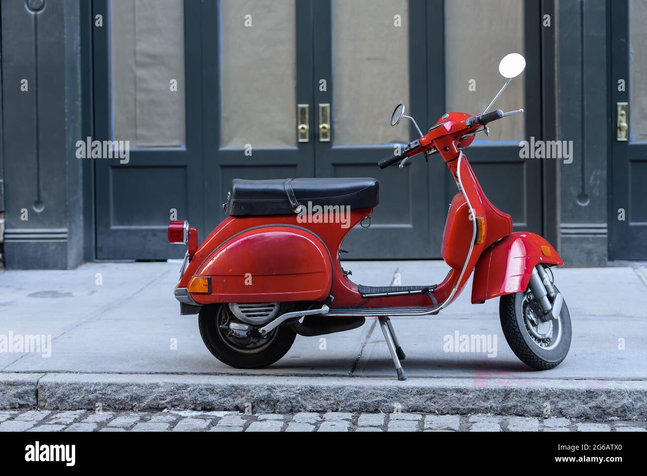 Small, red motor bike parked on a street in New York City. Stock Photo