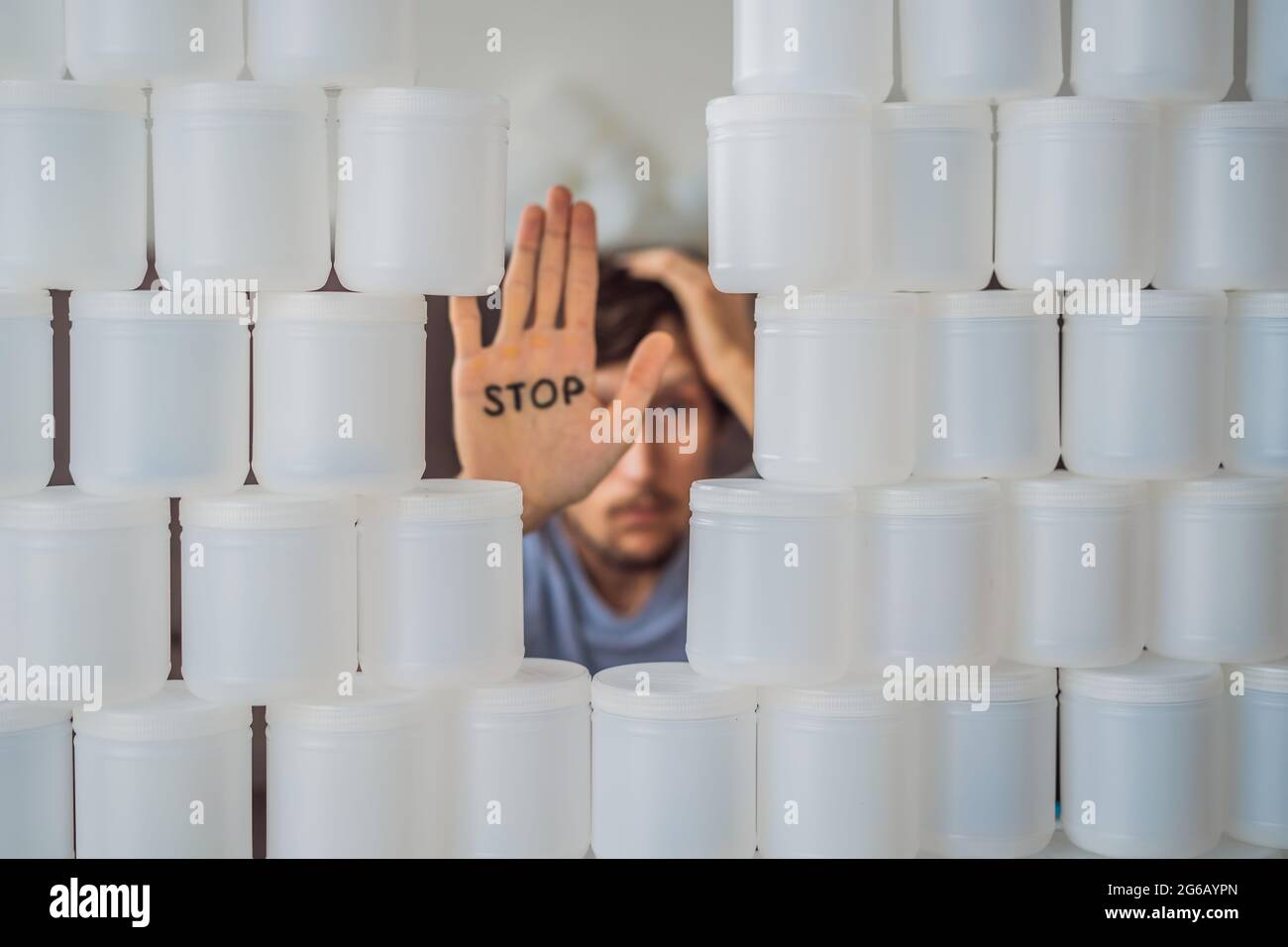 Man showing stop surrounded by many jars of yoghurt that he uses in a year. A huge amount of plastic food jars. Excessive consumption of plastic Stock Photo
