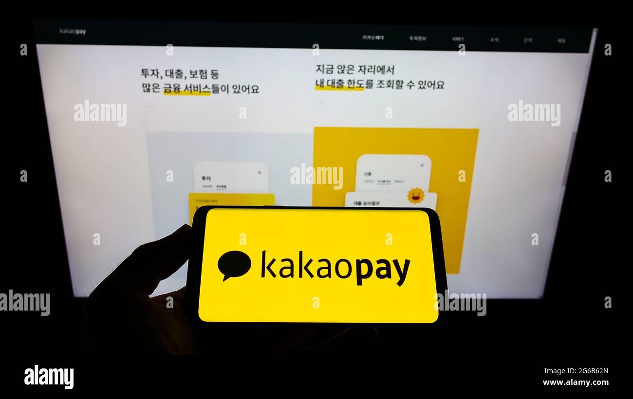 Person holding smartphone with logo of South Korean payment company KakaoPay Corp. on screen in front of website. Focus on phone display. Stock Photo