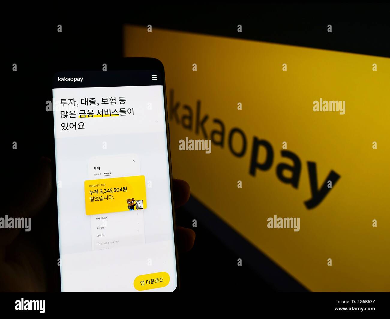 Person holding smartphone with website of South Korean payment company KakaoPay Corp. on screen in front of logo. Focus on center of phone display. Stock Photo