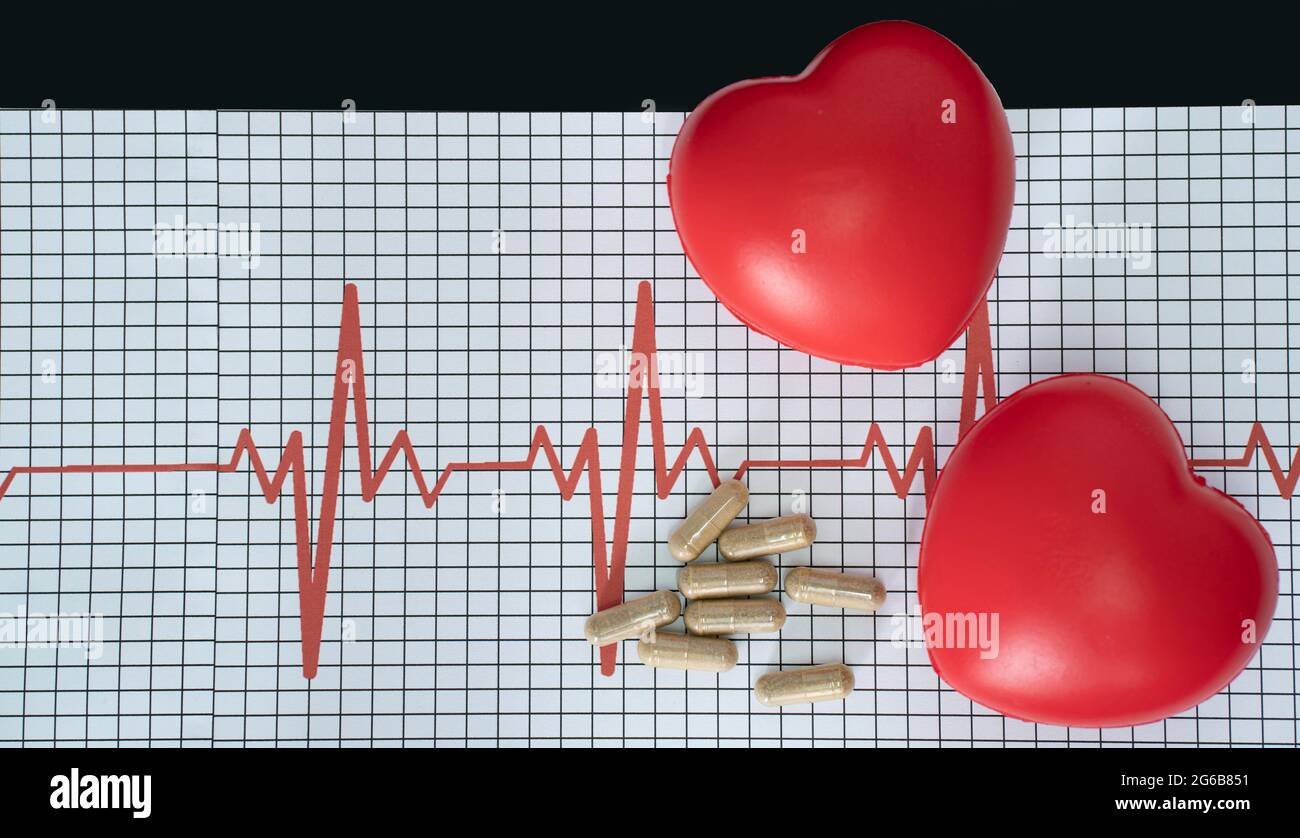 Layout of an electrocardiogram, some pills and two heart-shaped models on black background Stock Photo