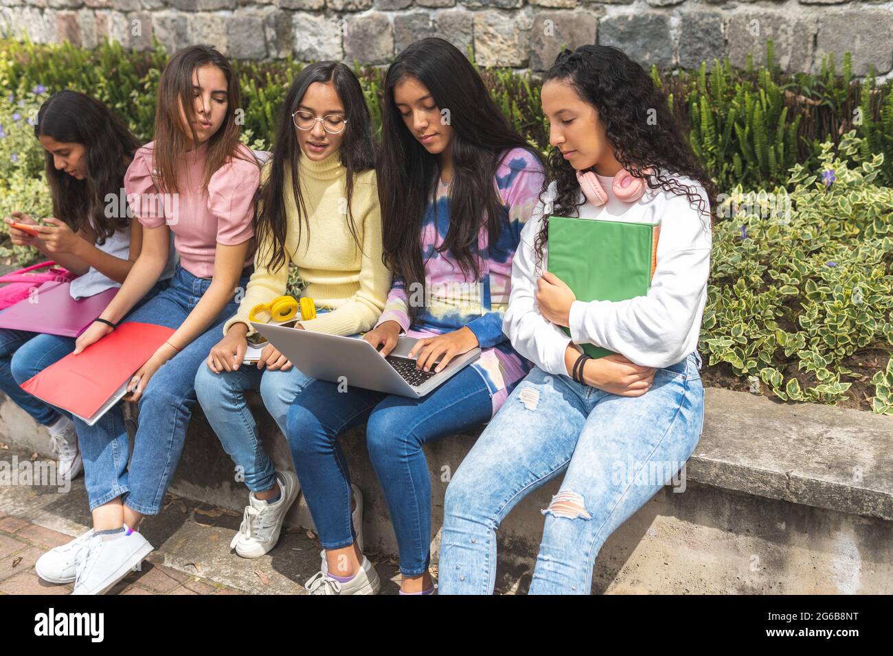 Group of Latina teenage student girls interacting with technology, laptop and cell phones at a bus stop. Stock Photo