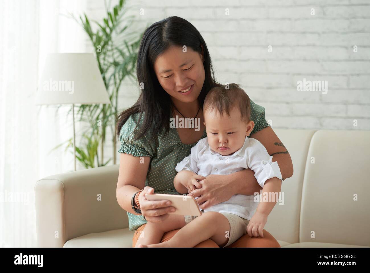 Smiling mother showing animated cartoon or educational video on smartphone  to her little son when sitting on sofa at home Stock Photo - Alamy