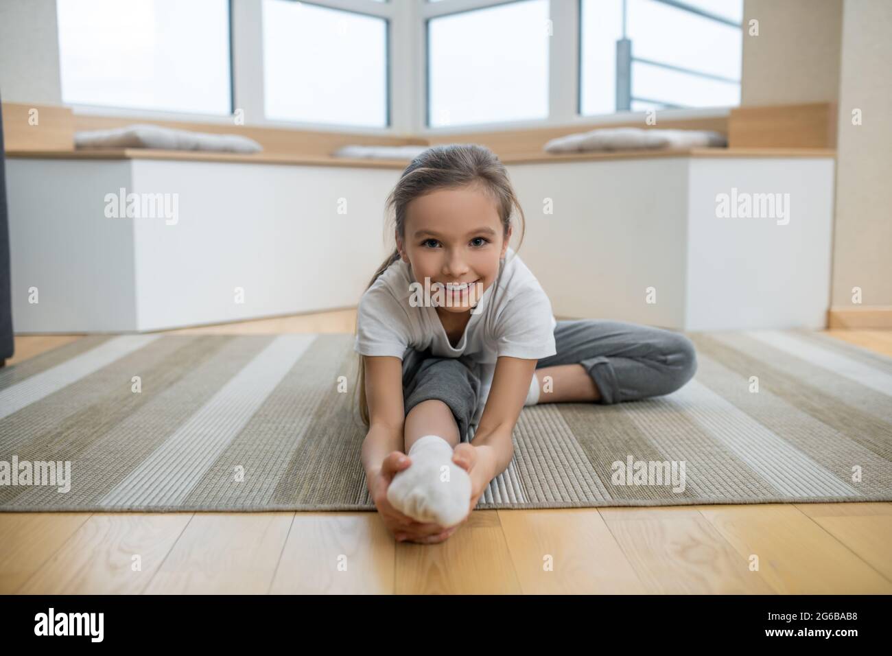 Cute girl sitting on the floor and stretching Stock Photo - Alamy