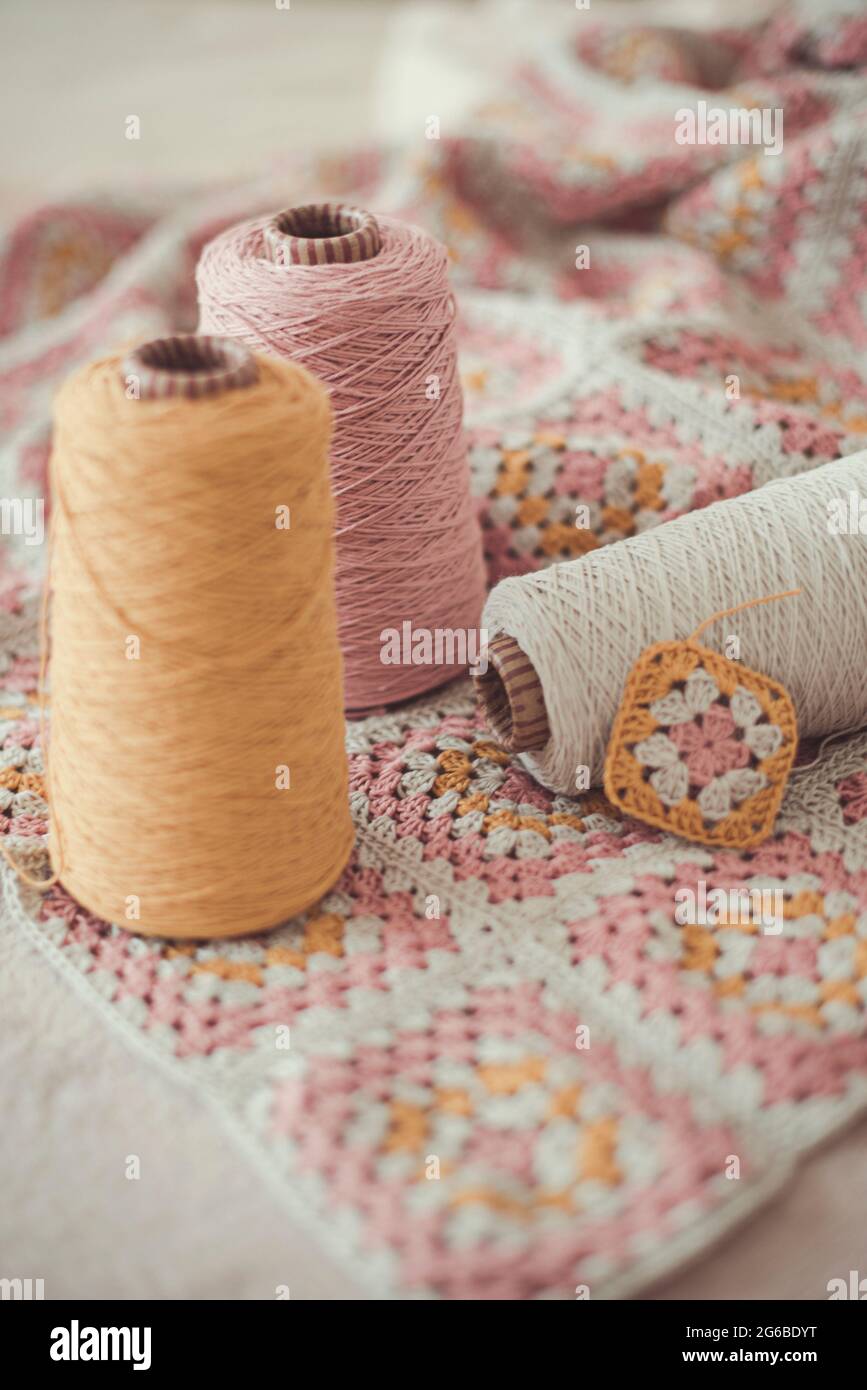 Close-up of three skeins of yarn and a crocheted patchwork blanket Stock Photo