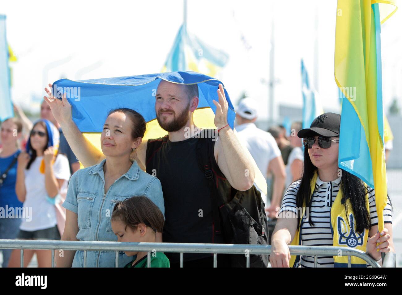 KYIV REGION, UKRAINE - JULY 4, 2021 - A man and a woman hide from the summer sun under a Ukrainian flag during the welcome ceremony of Team Ukraine at Stock Photo