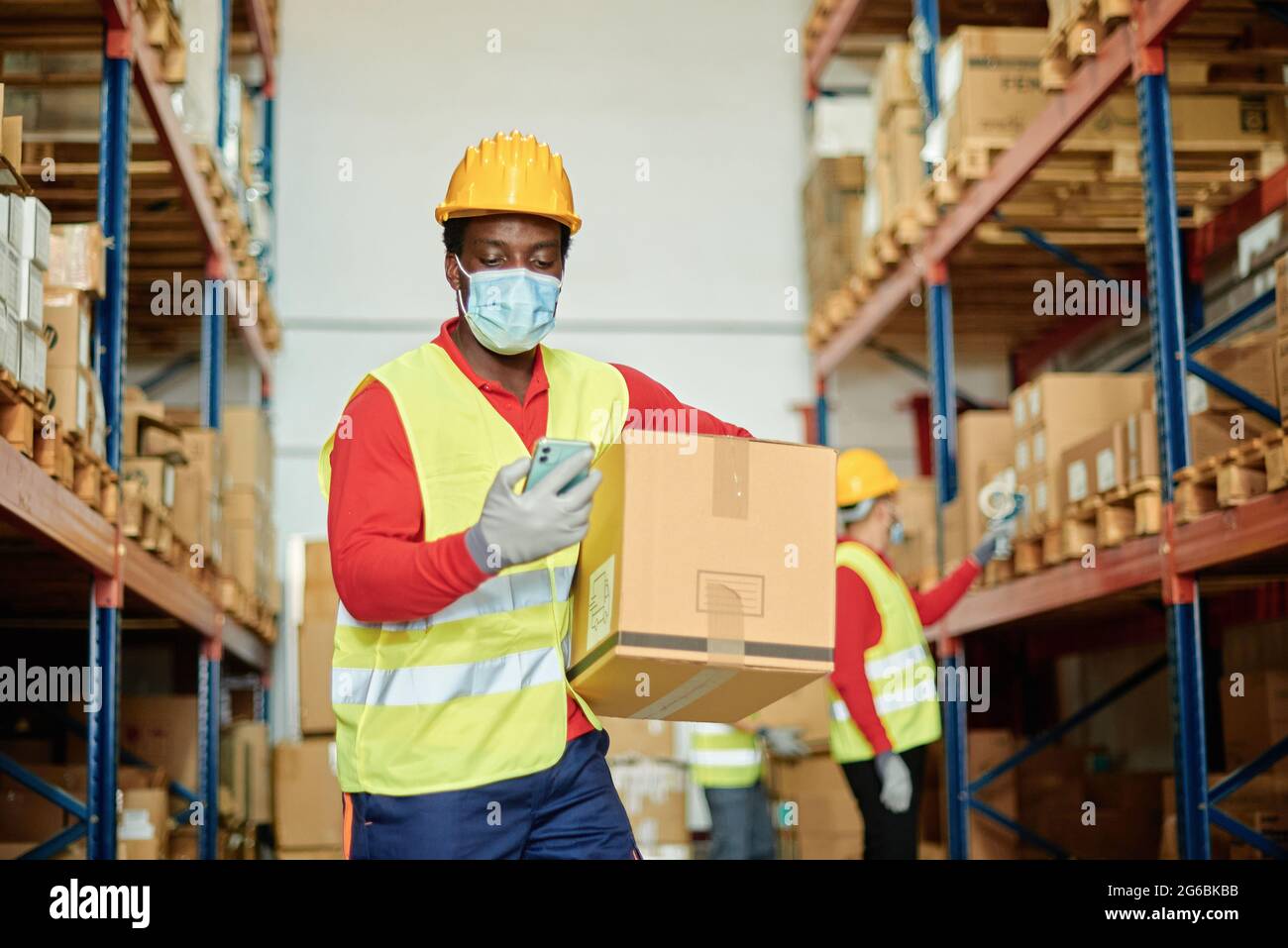 Male worker with box using smartphone in warehouse Stock Photo