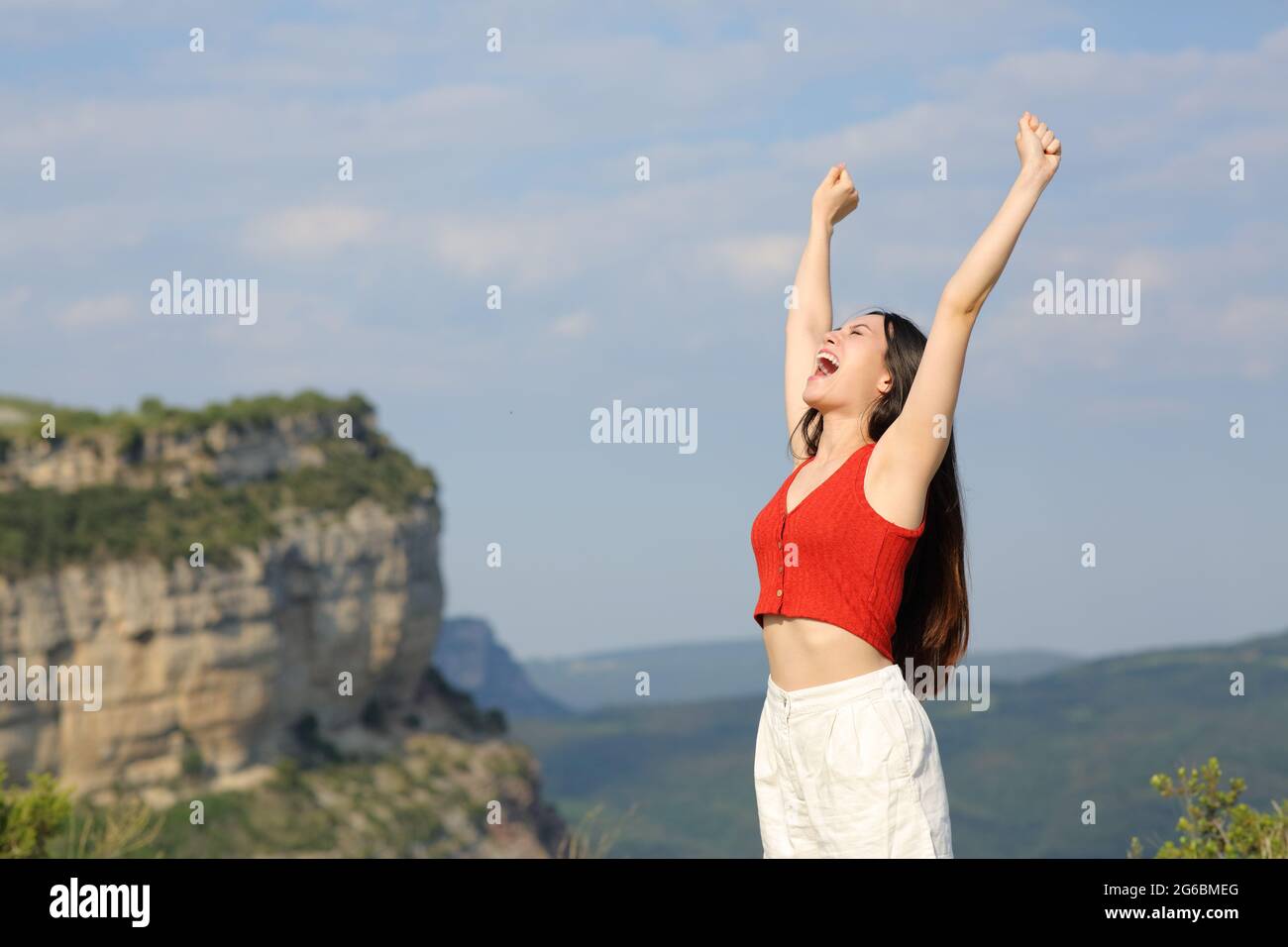 Excited asian woman celebrating raising arms in the mountain Stock Photo