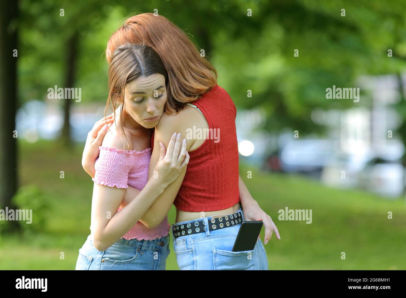 Woman spying her friend checking smart phone content in a park Stock Photo