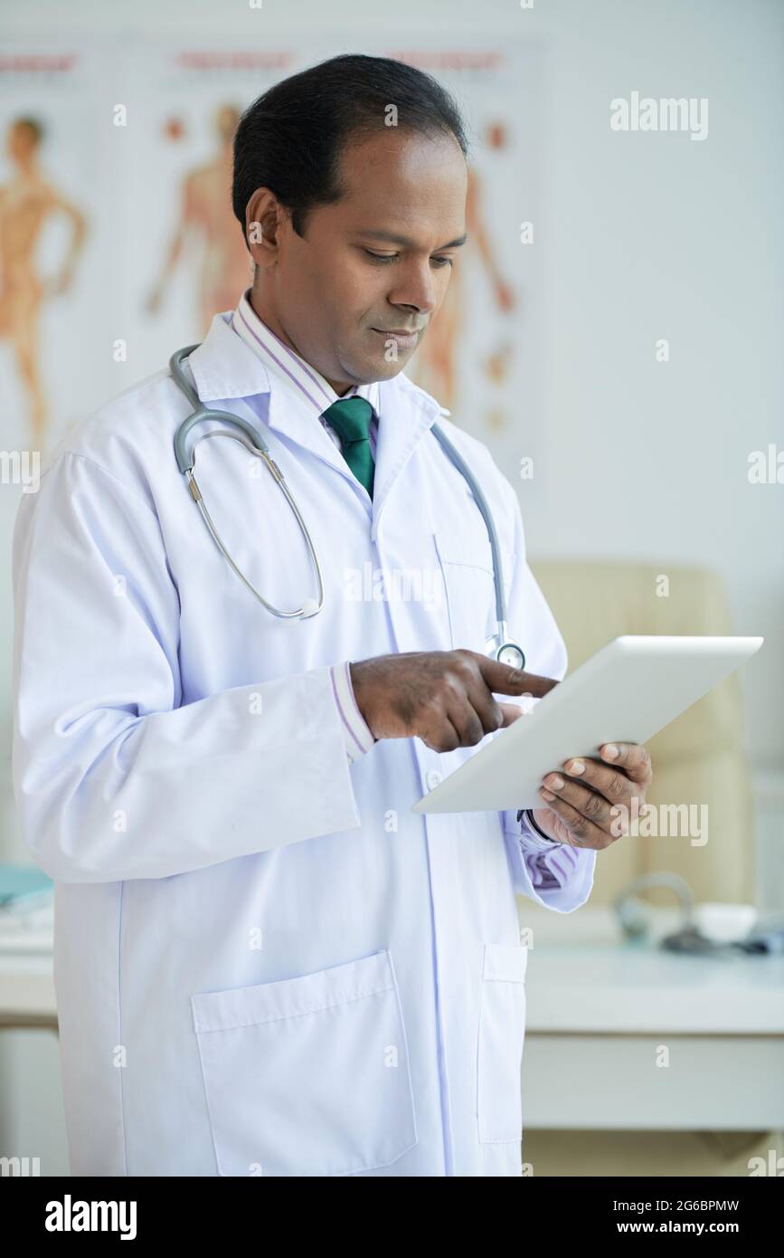 Serious confident physician reading anamnesis of patient on tablet computer Stock Photo