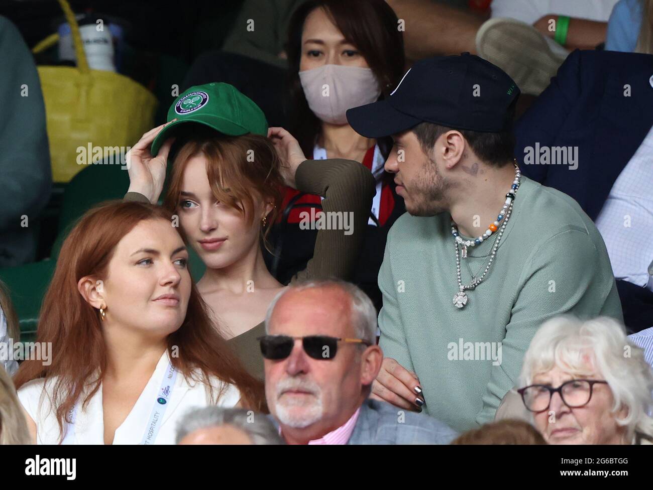 London, UK. 03rd July, 2021. Phoebe Dynevor puts on a cap alongside Pete Davidson watching Roger Federer v Cameron Norrie in the third round. Wimbledon Day Six Credit: Paul Marriott/Alamy Live News Stock Photo